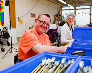Zwei Personen in einem Arbeitsraum mit blauen Kisten.